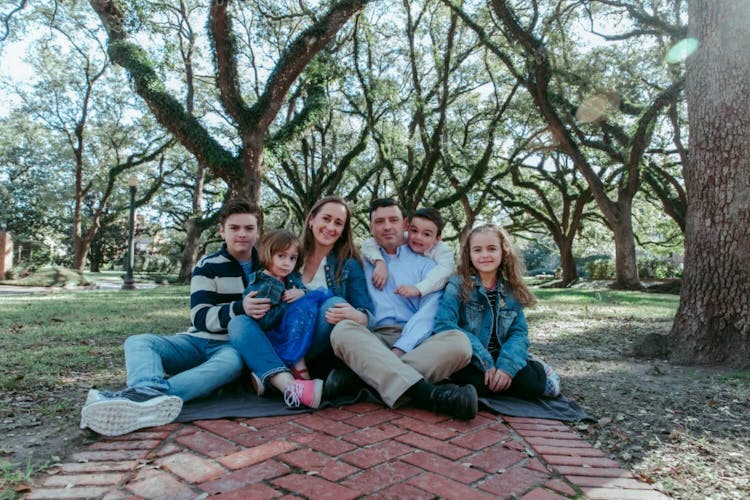 Family of five sitting on a brick path in a park