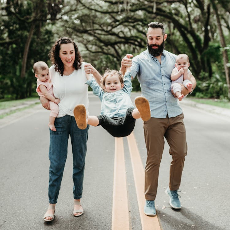 A family of four walking on a road, with the parents swinging their children by the arms.