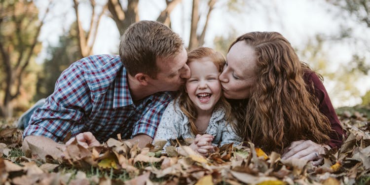 A family of four laughing together while lying in a pile of autumn leaves.