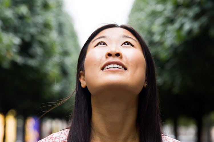 A woman looking up at the sky with trees in the background