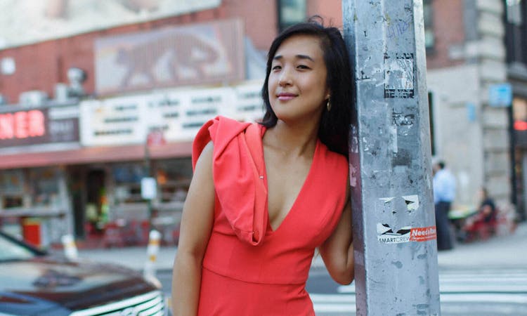 A woman in a red dress leaning against a street pole