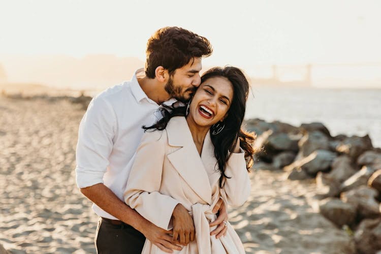 A couple embracing and laughing on the beach with the sun setting in the background