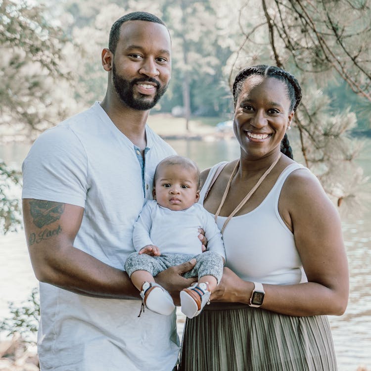 Family poses with their baby in front of a lake for their free outdoor family photoshoot