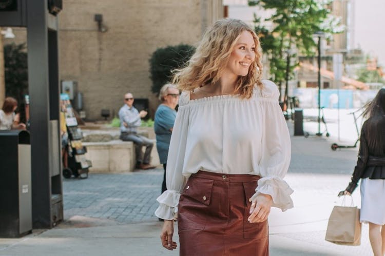 Smiling woman walking on a city sidewalk with outdoor seating in the background