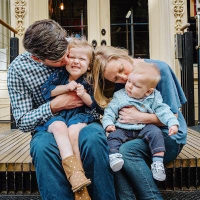 A happy family with two children sitting on steps outside their home.