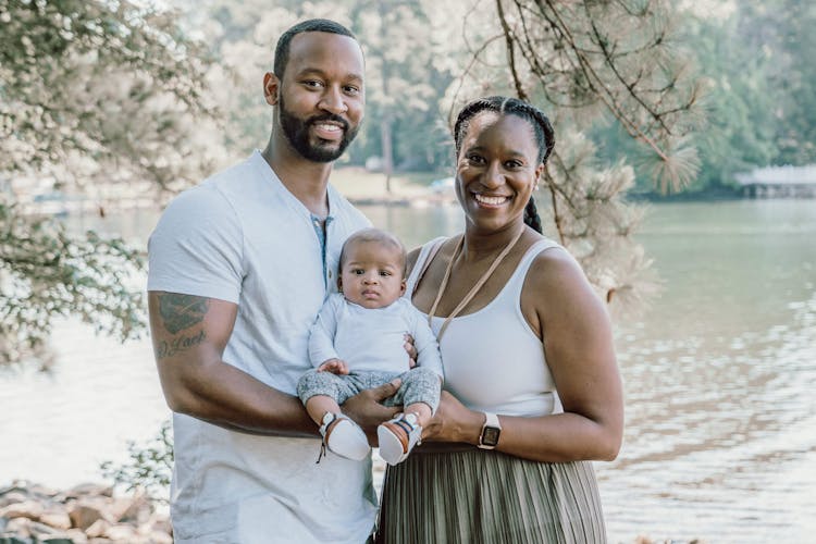 Couple holding a baby between them in a park with a lake in the background