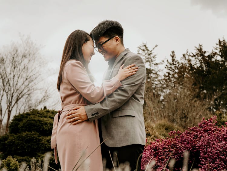 A couple touches foreheads lovingly surrounded by flowers.