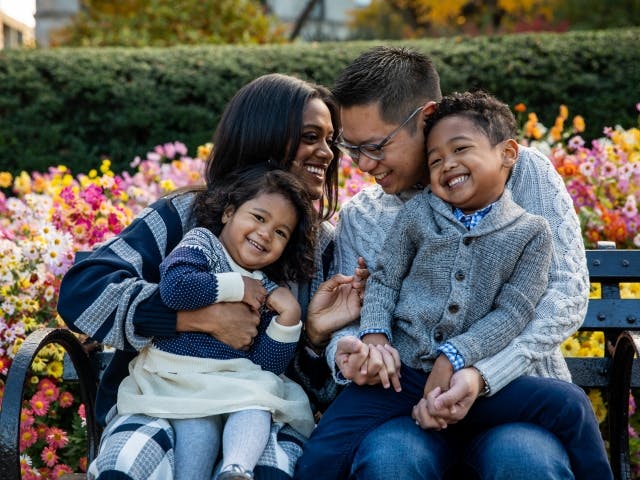 A happy family with two children enjoying time together on a park bench surrounded by colorful flowers.