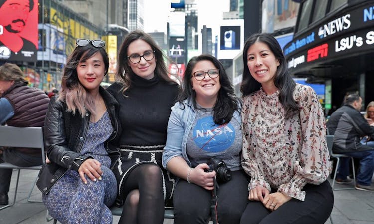 Four smiling women posing for a photo in Times Square.