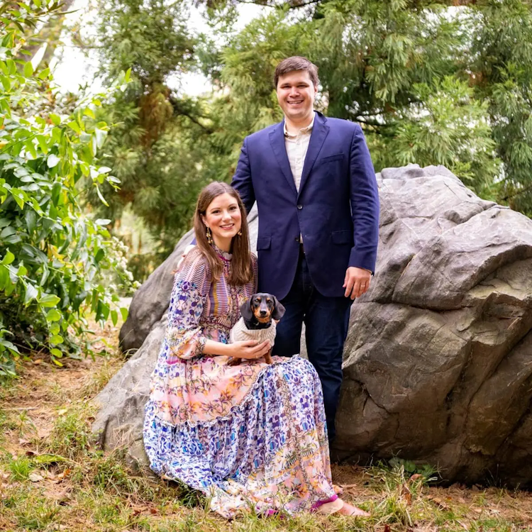 A smiling couple with a dog posing in a garden.