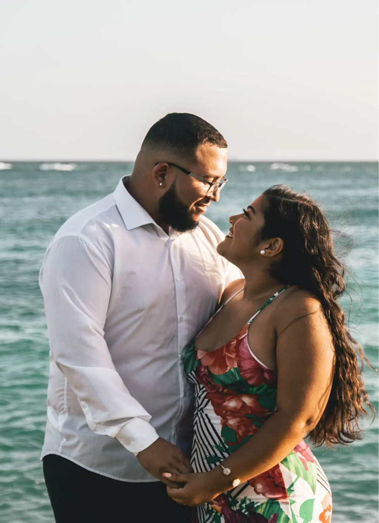 A couple holding hands and looking at each other affectionately by the sea.