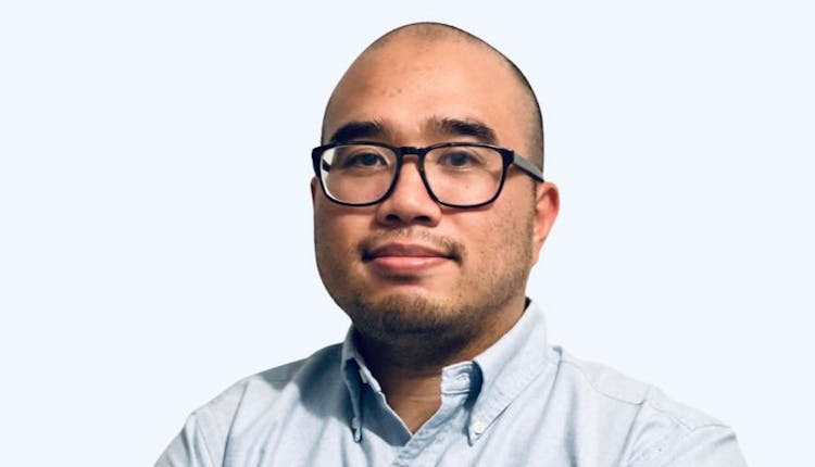 A portrait of a smiling man with glasses wearing a light blue shirt against a white background.