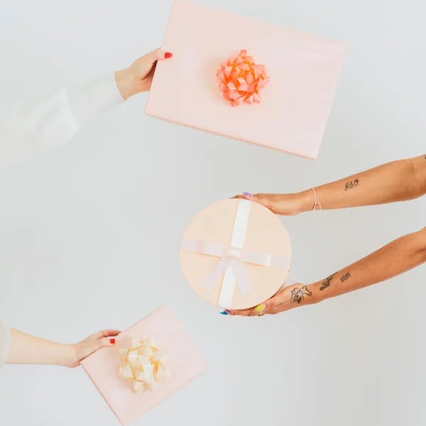 Four arms exchanging beautifully wrapped gift boxes on a simple background.