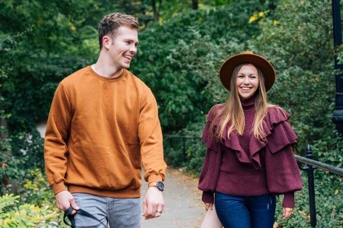 A smiling couple walking together through a park, the woman wearing a hat